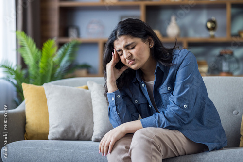 Fotografie Suffering from headache and pressure, Indian young woman sits on sofa at home an