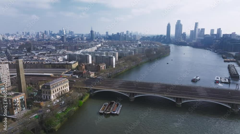 Aerial view of London showing the River Thames, the Shard, Canary Wharf, railway tracks, residential areas, and boats under a clear sky. Aerial view of London showing the River Thames, the Shard, Canary Wharf, railway tracks, residential areas, and boats under a clear sky.