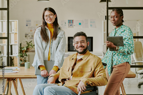 Portrait of smiling team lead with disability surrounded by his beautiful biracial colleagues in office