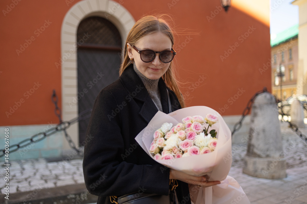 A young woman with sunglasses smiling while holding a bouquet of flowers outside a historic building. She appears joyful and the scene captures a beautiful moment in the city.