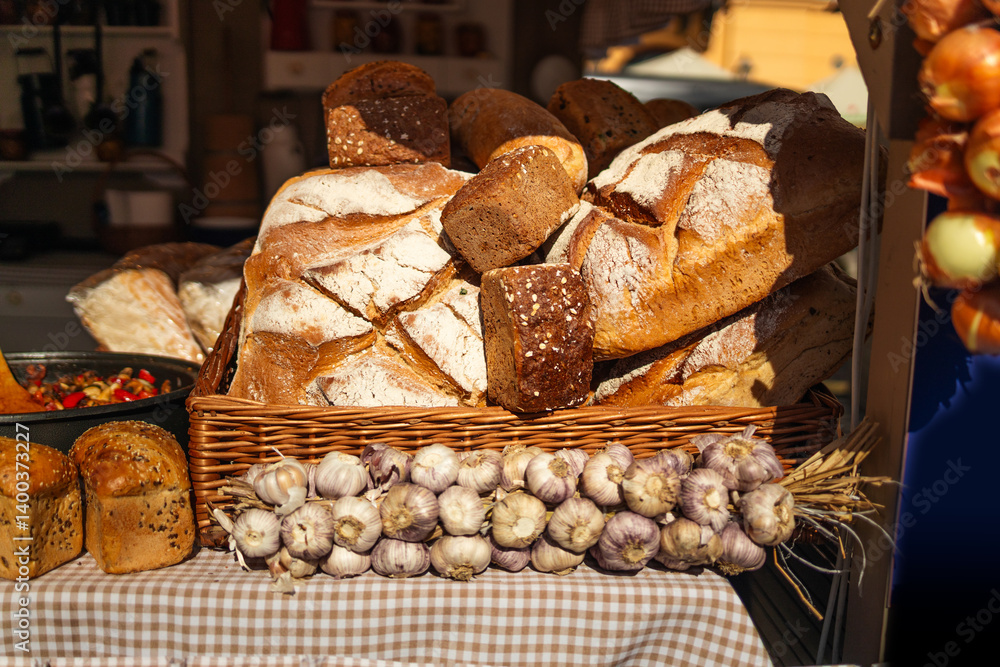 A variety of freshly baked loaves of bread are neatly arranged on a display table at a market. The loaves are golden-brown with crisp crusts and sit in a basket with a checkered cloth. Lights hang