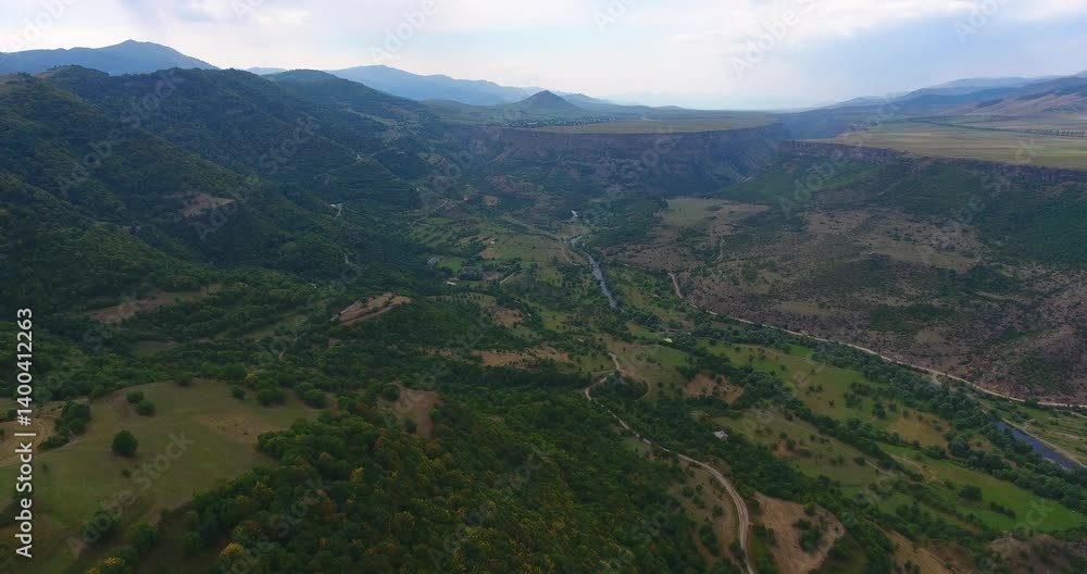 Aerial scenery of a lush valley with rolling hills and trails under cloudy sky Aerial scenery of a lush valley with rolling hills and trails under cloudy sky
