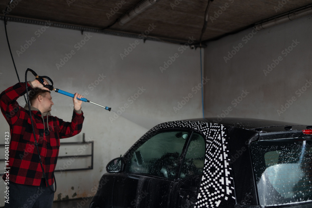 A man with a beard washes a gray car with a high-pressure washer in a car wash. Expensive advertising photography