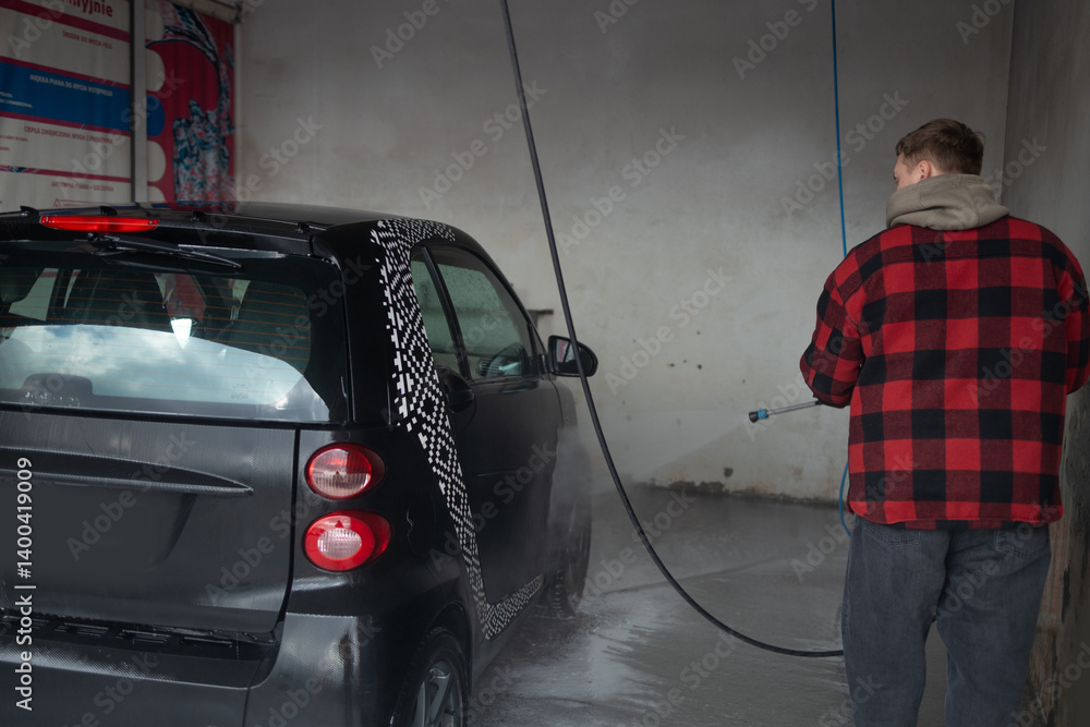 A man with a beard washes a gray car with a high-pressure washer in a car wash. Expensive advertising photography
