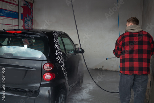 Obraz na płótnie A man with a beard washes a gray car with a high-pressure washer in a car wash. Expensive advertising photography w salonie