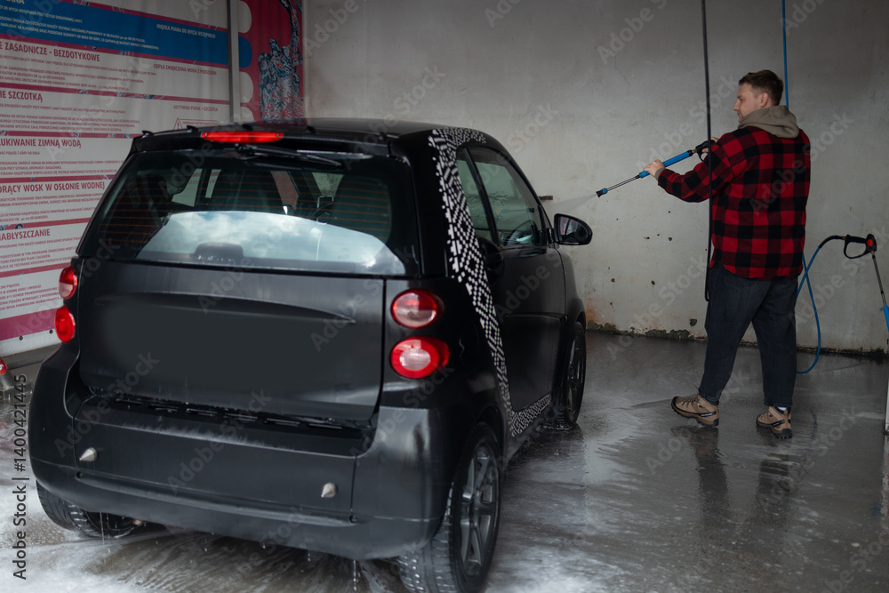 A man with a beard washes a gray car with a high-pressure washer in a car wash. Expensive advertising photography