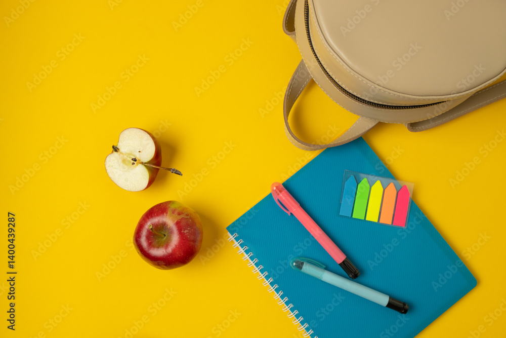 A vibrant and colorful setup featuring office supplies such as pens, sticky notes, and a notepad, complemented by a fresh red apple. The bright yellow background adds an energetic touch to the scene