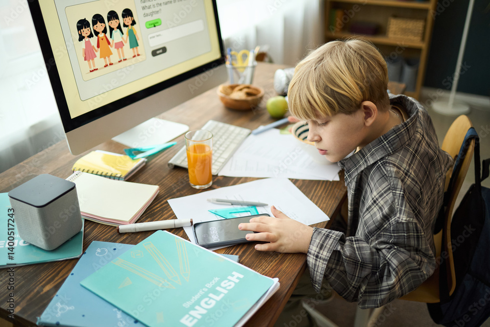Young boy engaged in studying at desk with various educational tools surrounding him. Computer screen, notebooks, and juice glass on desk Young boy engaged in studying at desk with various educational tools surrounding him. Computer screen, notebooks, and juice glass on desk