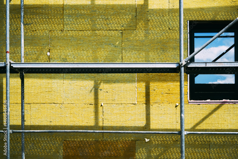 Obraz premium Mineral wool house insulation. Construction site with scaffolding and high-density slab insulation product installation on building facade.