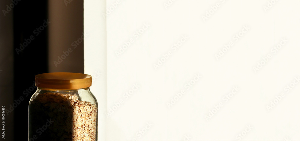A minimalistic scene featuring a jar of oatmeal against a clean white background, with subtle shadows adding depth to the composition. Banner for design with copy space
