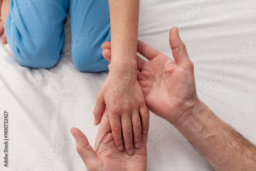 The child's hand is covered with red spots. The doctor examines the child's hand. The concept of rubella or atopic dermatitis