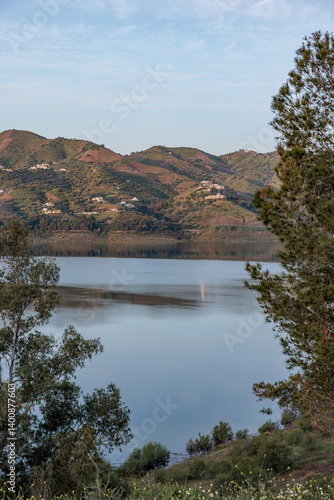 Guadalhorce reservoir reflecting the hills at sunset with trees framing the scene