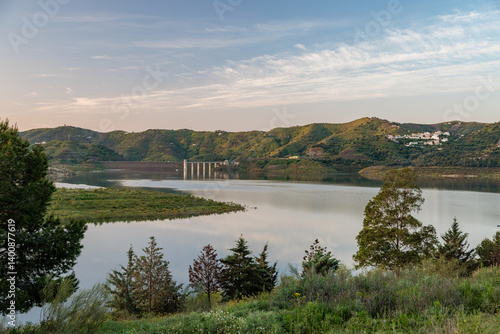 Calm lake reflecting sunset light with bridge and hills in background