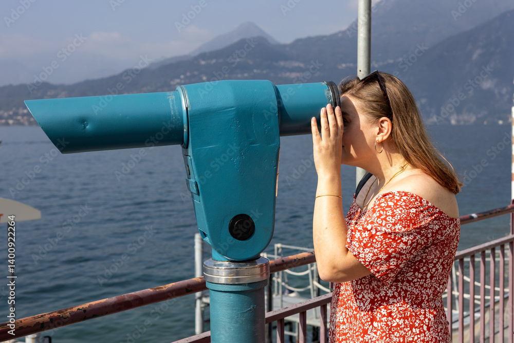 Young 30s woman looking through a coin operated binoculars. Como Lake, Italy.