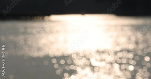 Light bokeh from out of focus sunset light reflection over the water surface inside pond in the garden park in the evening.