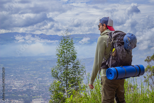 An adventurer in rugged outdoor gear stands on a hilltop, surveying a sweeping valley with distant peaks under a dramatic, cloudy sky. Ideal for adventure and exploration themes.