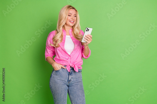Obraz na płótnie Young blonde woman in pink shirt casually posing with smartphone in hand on gree