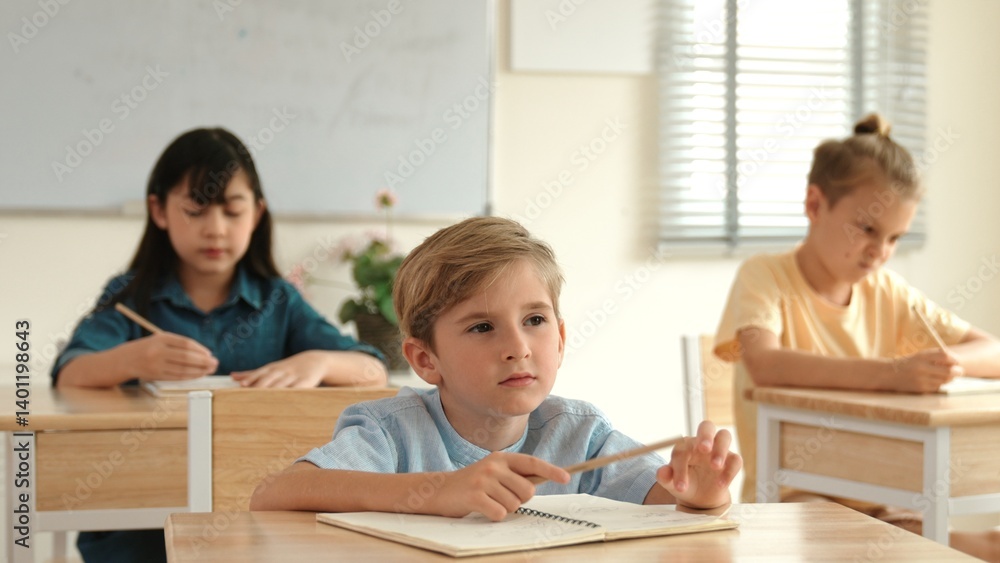 Caucasian boy looking at blackboard while diverse skilled student learning at school and taking a note. Smart child in casual cloth sitting in front of blackboard while children doing test. Pedagogy. Caucasian boy looking at blackboard while diverse skilled student learning at school and taking a note. Smart child in casual cloth sitting in front of blackboard while children doing test. Pedagogy.