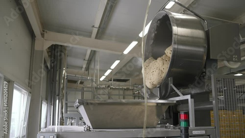 Industrial mixer pouring fresh dough into stainless steel container, showcasing automated food processing within modern bakery production line
