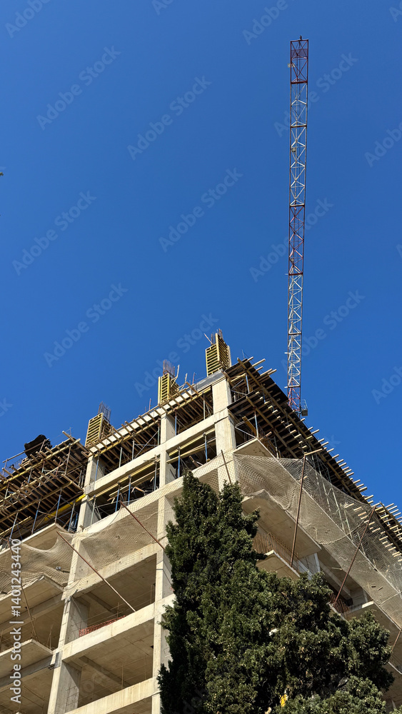 Close-up angled view of high rise building under construction with crane arm reaching into the sky.