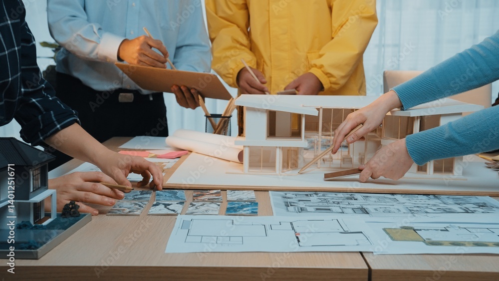 A diverse team of professionals engages in an architectural design meeting, reviewing blueprints and 3D models in a bright, modern workspace. SACTR