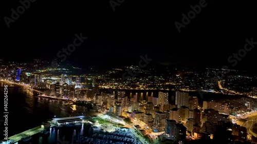 A stunning aerial view of a vibrant city skyline beautifully illuminated at night by the Mediterranean coast