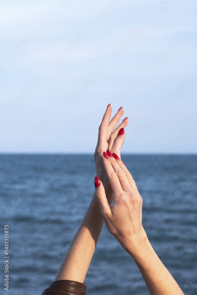 Elegant hands with red nails against ocean horizon background Elegant hands with red nails against ocean horizon background