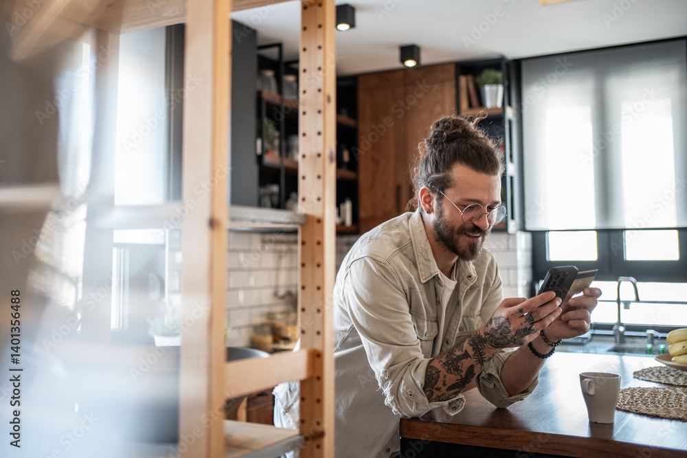 Freelancer smiling and shopping online using smartphone and credit card in kitchen