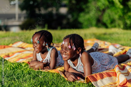 Two happy young black twin sisters lying on blanket in park