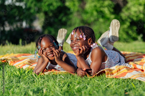 Two african girls lying on blanket in park smiling and having fun