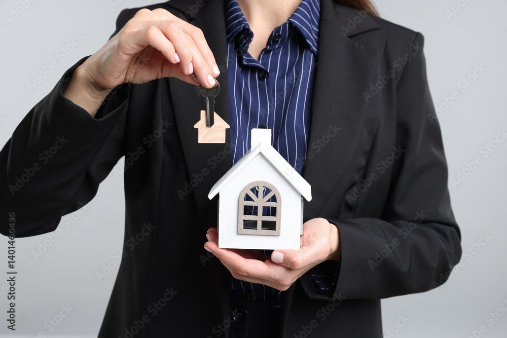 Real estate agent holding key with keychain and house model on light grey background, closeup Real estate agent holding key with keychain and house model on light grey background, closeup