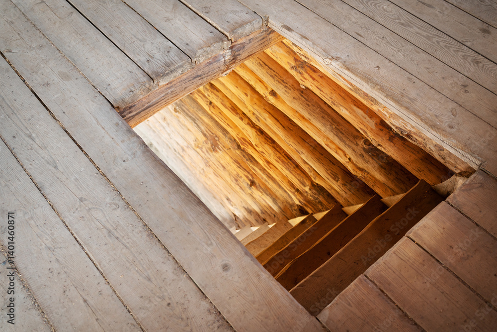 Old wooden flooring with a square hole revealing rustic log stairs leading downwards Old wooden flooring with a square hole revealing rustic log stairs leading downwards