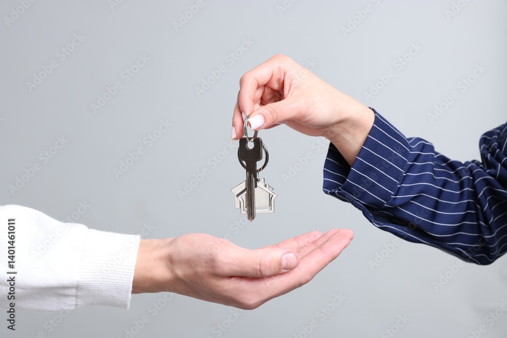 Real estate agent giving house key to new owner on gray background, closeup Real estate agent giving house key to new owner on gray background, closeup