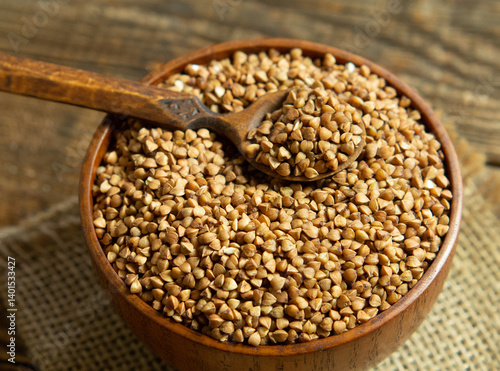 Organic buckwheat groats in a wooden bowl with a spoon on a linen napkin on a wooden table.