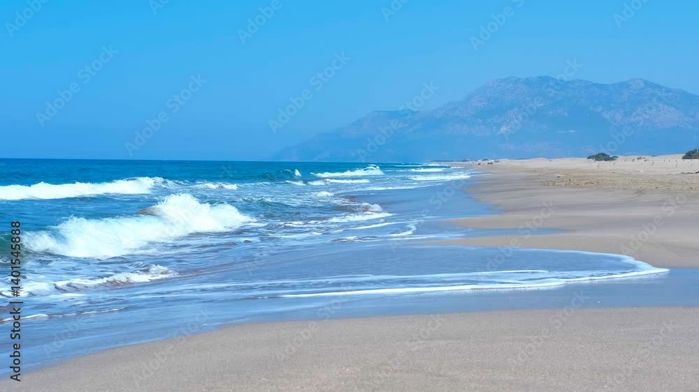 Turquoise sea gently lapping on the shores of beach. Turquoise waves rolling onto the pristine sands of beach create a serene atmosphere, framed by a stunning mountain range under a clear blue sky Turquoise sea gently lapping on the shores of beach. Turquoise waves rolling onto the pristine sands of beach create a serene atmosphere, framed by a stunning mountain range under a clear blue sky