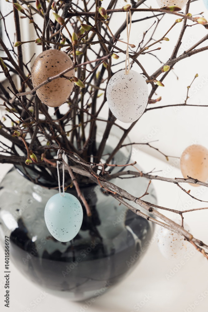 Easter tree decorated colorful pastel white and beige eggs. Birch branches with hang eggs in vase on white table. Close up. Vertical format.