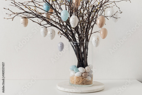 Easter tree decorated colorful pastel white and beige eggs. Birch branches with hang eggs in vase on white table. Copy space. Home white interior.