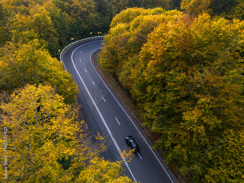 Fototapeta Naklejka Na Ścianę i Meble -  vibrant autumn colors of a forest with a winding asphalt road, aerial view