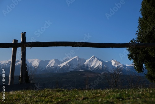 Snow-capped peaks of High Tatras and Bialskie Tatras mountains in frame of wooden fence, Pass over Lapszanka, Poland