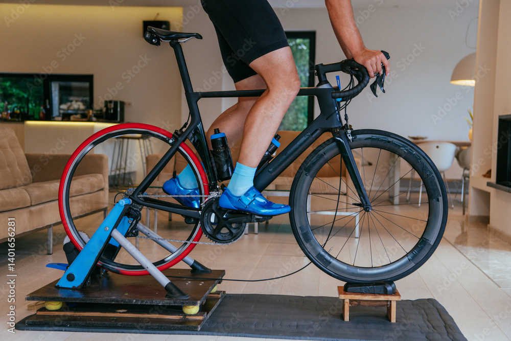A triathlete riding a triathlon bike on a machine simulation in a modern living room. Training during pandemic conditions.