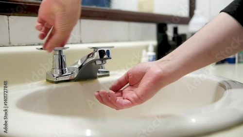 Bathroom sink water service is suspended, two hands turning on the sink faucet, a topic of water savings and consumption