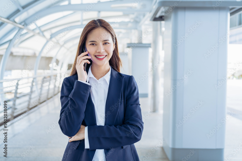 Smiling asian businesswoman talking on the phone while standing in front of modern business building, Concept of using the phone to communicate anywhere. Smiling asian businesswoman talking on the phone while standing in front of modern business building, Concept of using the phone to communicate anywhere.