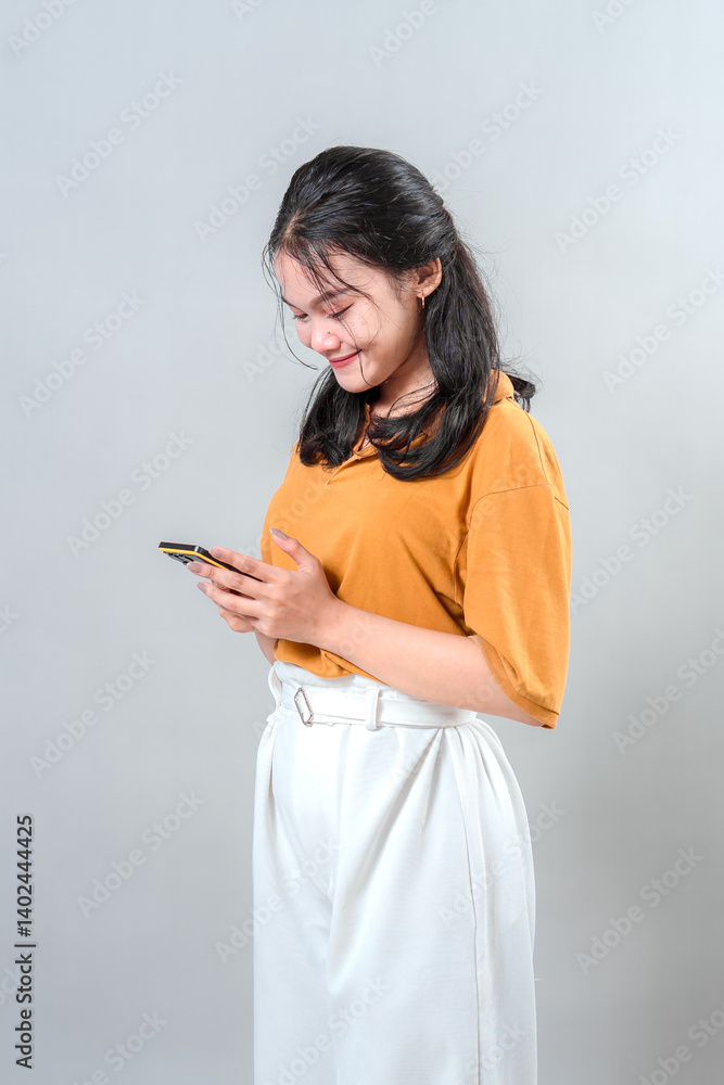 Young Asian woman smiling gently while looking down at her smartphone. Her expression reflects joy and calmness, perfect for mobile technology, lifestyle, or digital communication ads. Young Asian woman smiling gently while looking down at her smartphone. Her expression reflects joy and calmness, perfect for mobile technology, lifestyle, or digital communication ads.