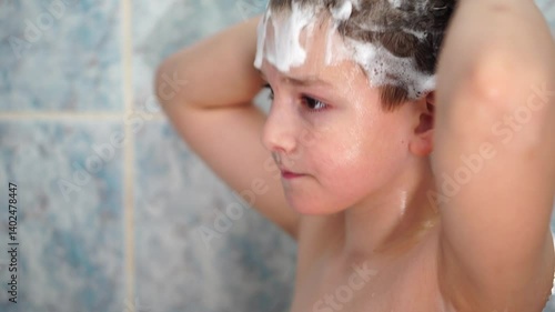 Teenage boy soaping his head with shampoo standing in the bathroom close-up