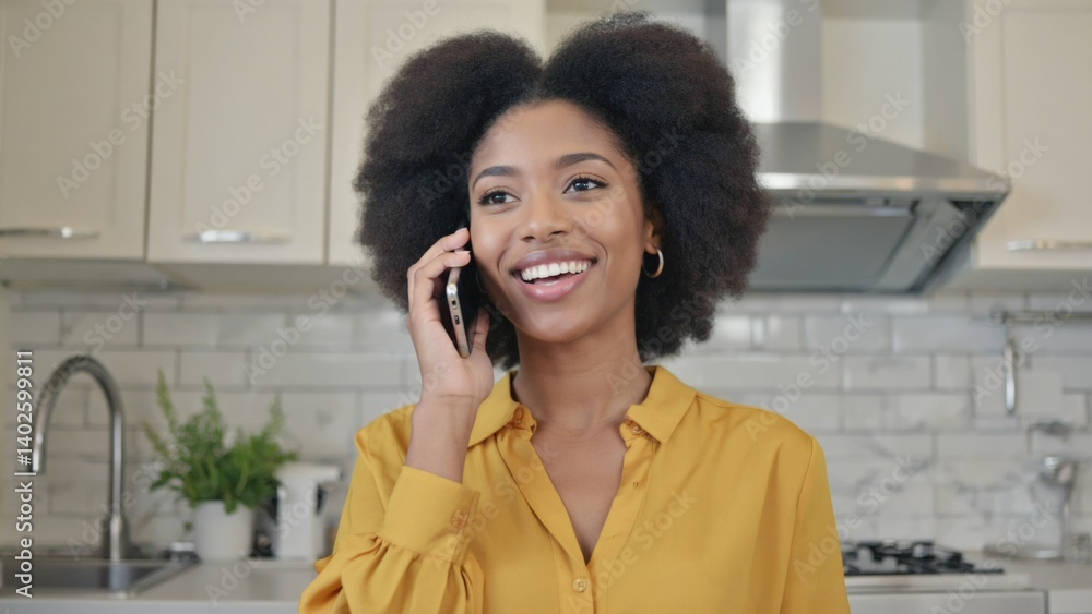 A smiling African American woman engaging in a conversation on her cell phone, standing in a well-equipped kitchen.