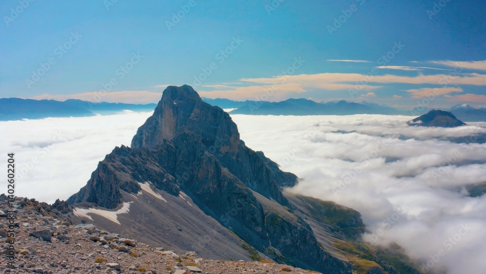 Early morning sunlight on a mountain peak, with clear skies and clouds below. The landscape is part of the Alps, suggesting an adventure hike in a scenic wilderness area.