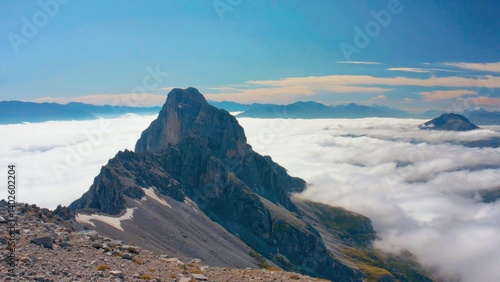 Obraz na płótnie Early morning sunlight on a mountain peak, with clear skies and clouds below. The landscape is part of the Alps, suggesting an adventure hike in a scenic wilderness area. w salonie