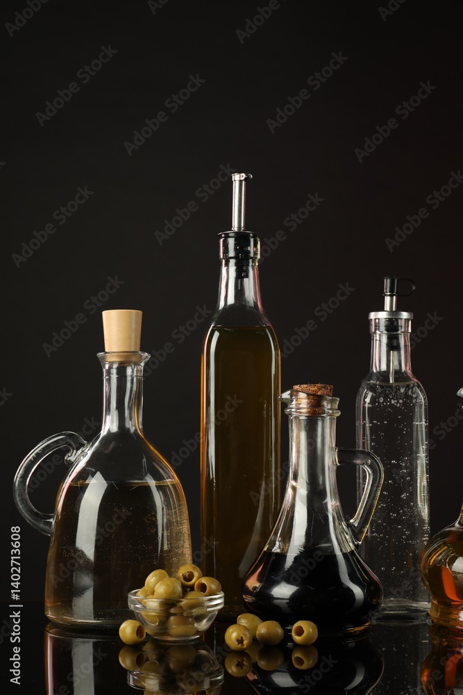 Obraz premium Salad dressings and olives on mirror surface against black background
