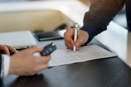Fotografie Closeup shot of customer signing contract and salesman holding car keys in a dea
