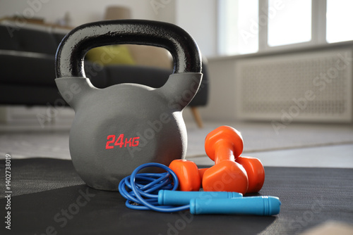 Kettlebell, jumping rope and dumbbells on fitness mat at home